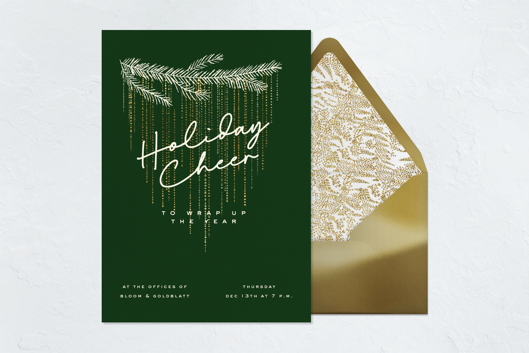 A dark green invitation beside a gold envelope reads, in script, “Holiday cheer” followed by “to wrap up the year” with an illustration of a white fir tree branch dripping with gold “tinsel” dots.