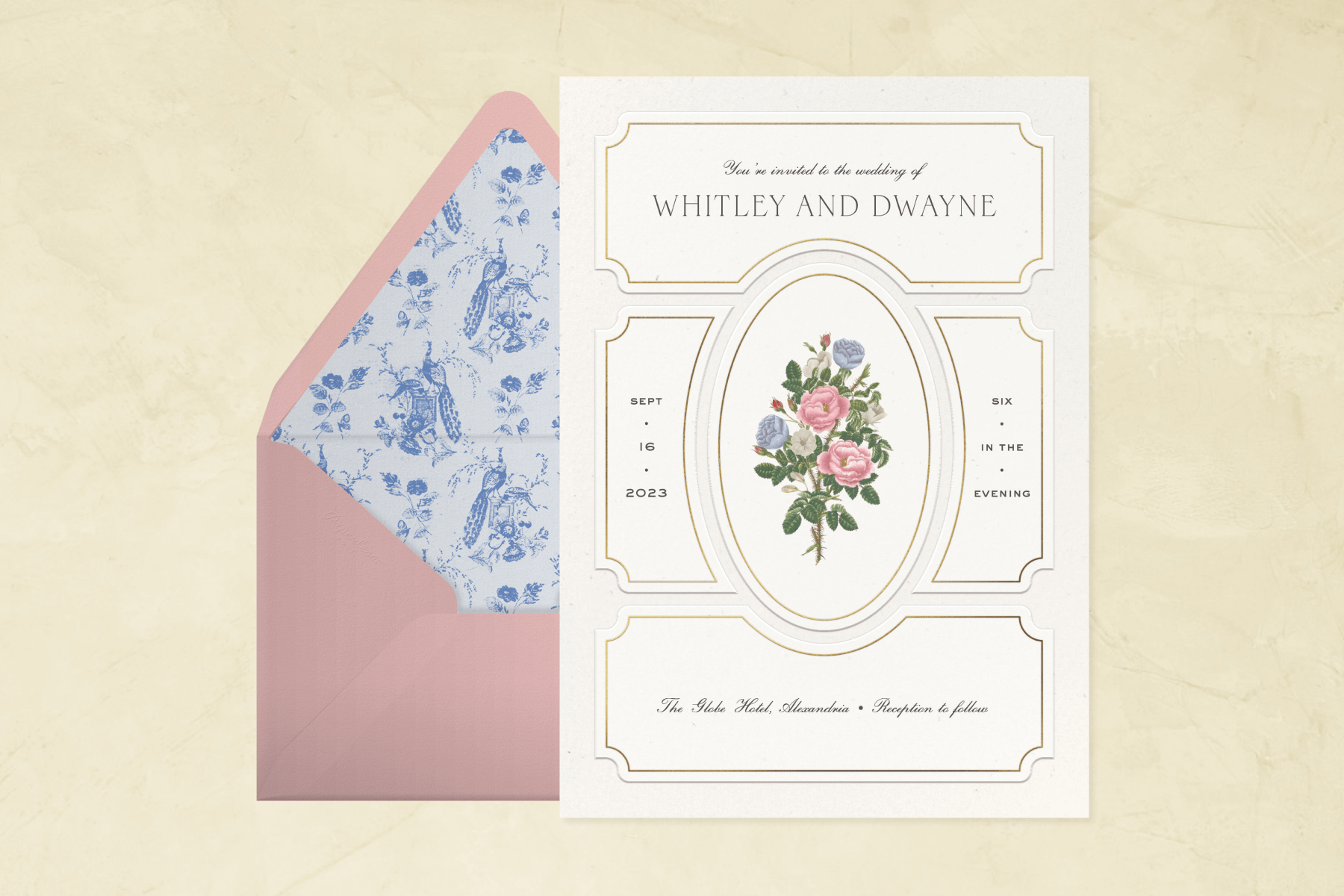 A white wedding invitation with picture frame molding-inspired shapes and an oval in the middle framing a bouquet of colorful roses and a pink envelope with a blue toile lining.