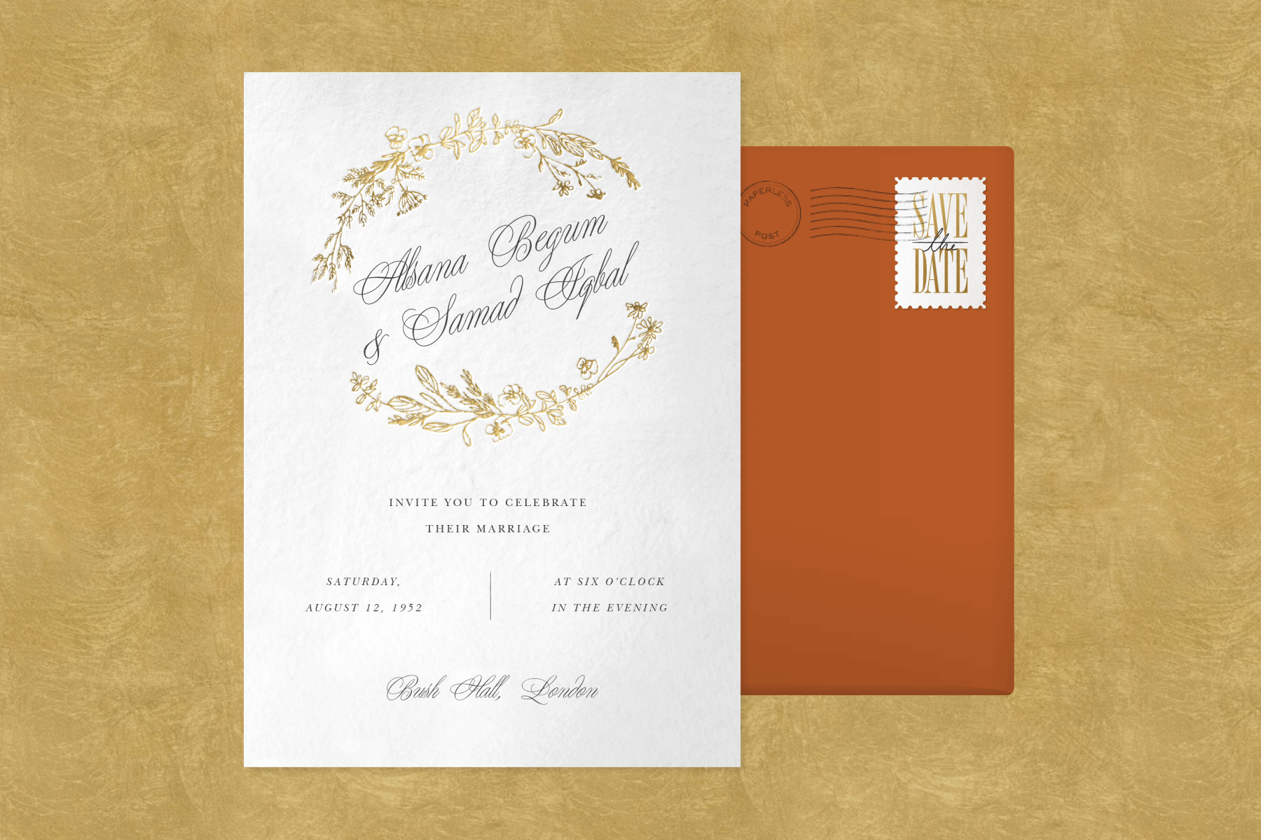 A white wedding invitation with gold sprigs circling the couple’s names written in script with an orange envelope and a stamp.