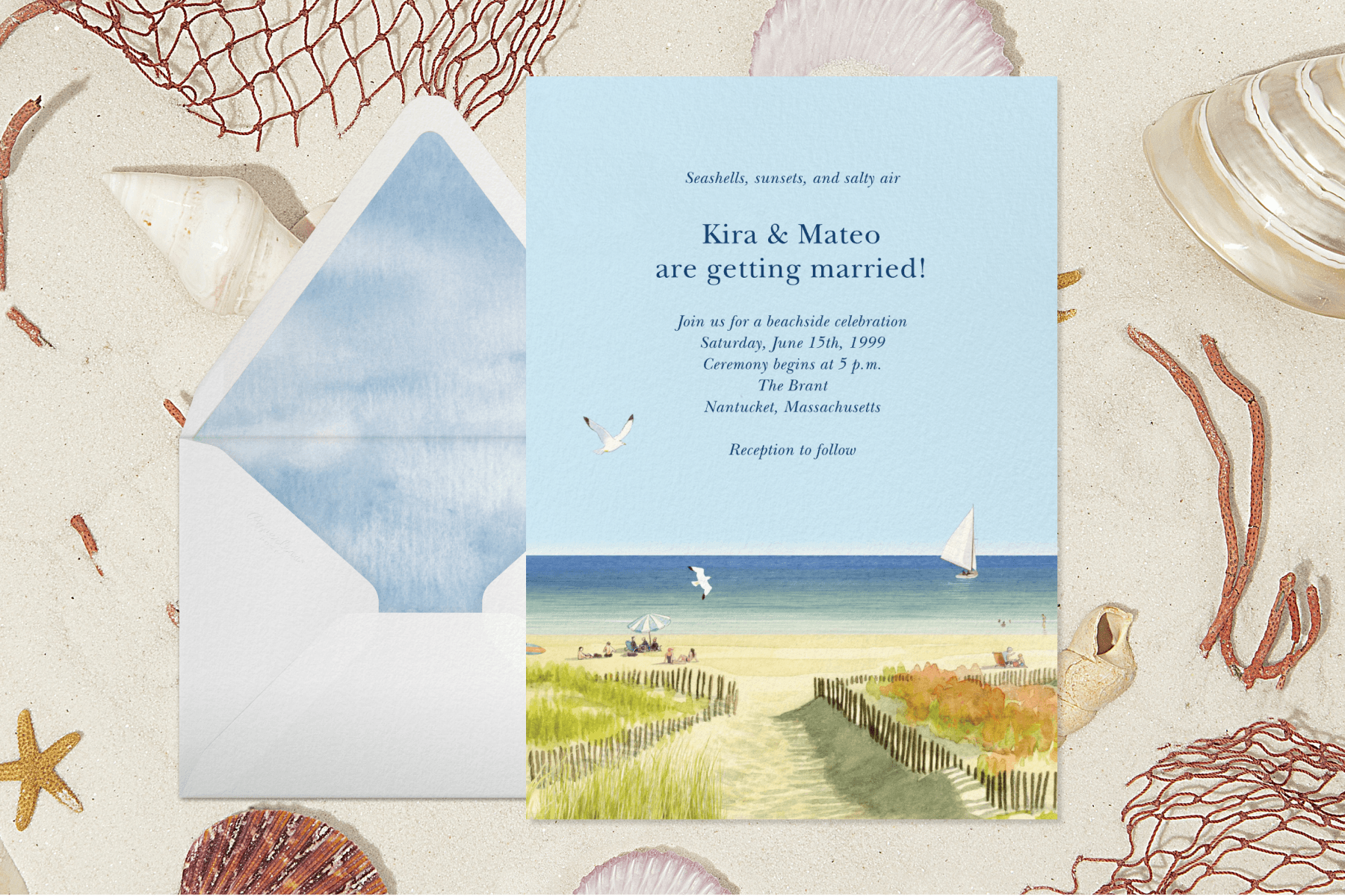 On a backdrop designed to look like a sandy beach sits a beach-themed wedding invitation next to a white envelope with blue and white lining.