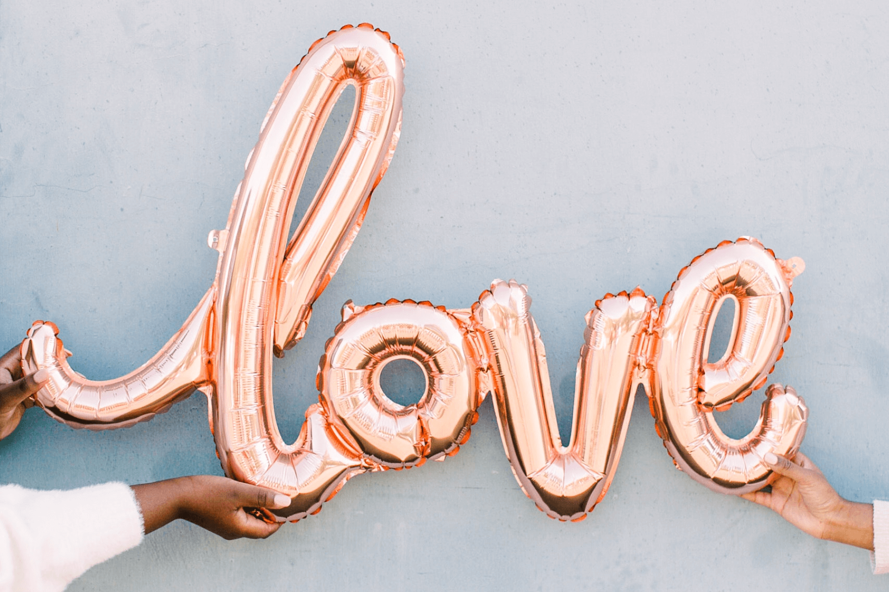 Hands hold up a pink mylar balloon that reads “love” in script.