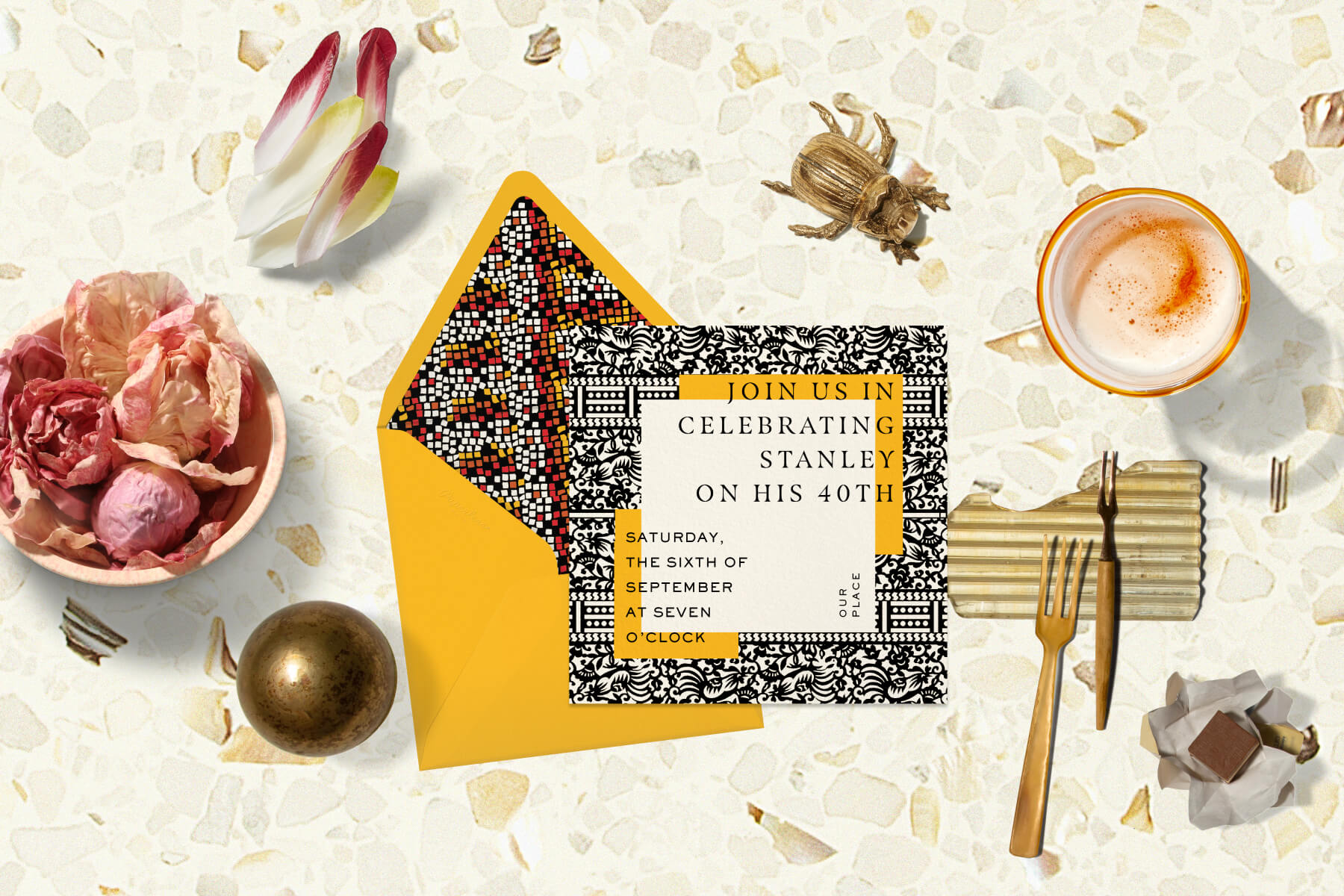 A Duro Olowu digital invitation with a black, white, and yellow patterned frame and a matching yellow envelope with a black, white, red, and yellow geometric pattern. The invitation is surrounded by objects like a brass ball, a cocktail, forks, and lettuces.