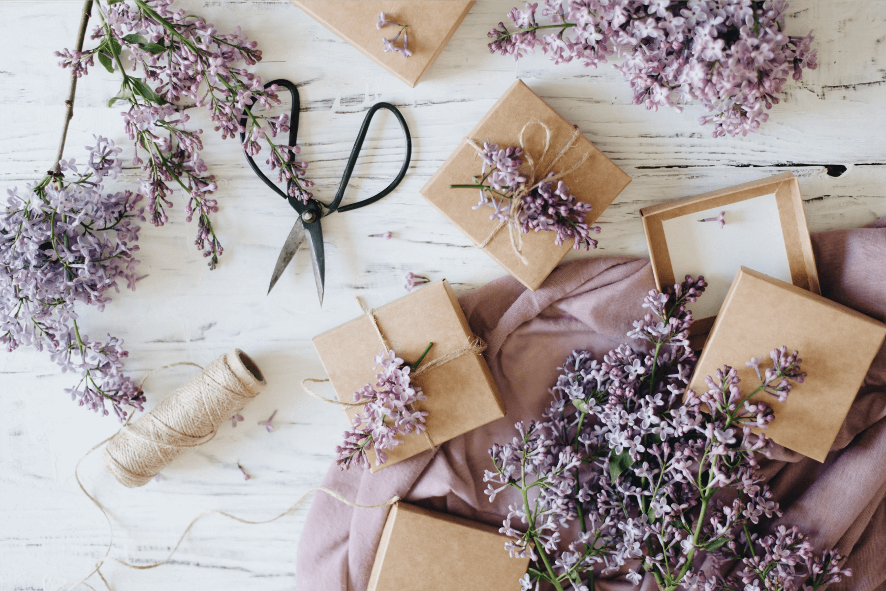 Lilac clippings on a table, some tied onto small brown gift boxes.