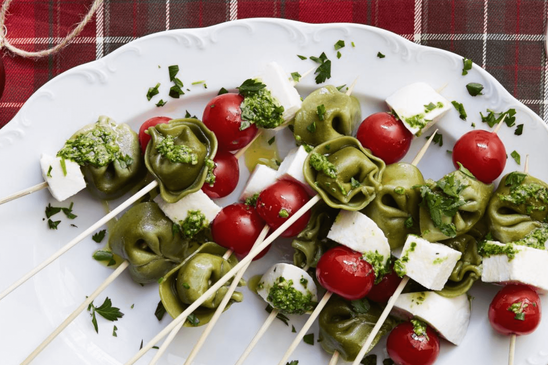 Skewers with green tortellini, red cherry tomatoes, and cubes of white cheese sprinkled with pesto.