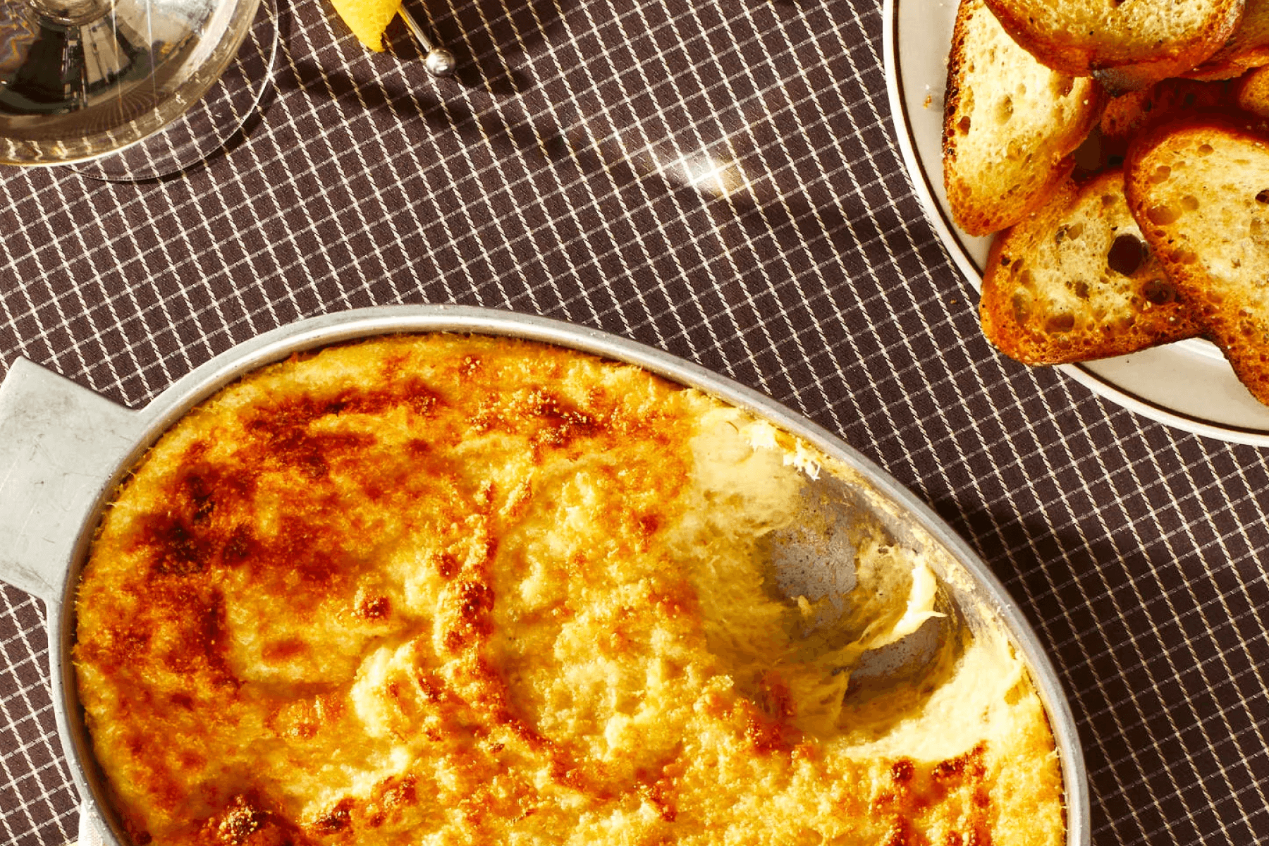 An oval dish with something baked and cheesy inside, beside a dish of sliced toast.