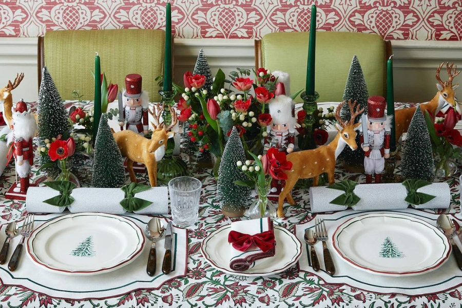 A maximalist Christmas-themed table setting with miniature pine trees, nutcracker dolls, and deer.