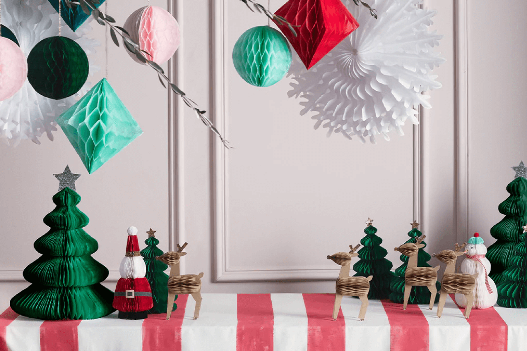 Paper Christmas decorations laid out on a red and white striped table with hanging paper decorations above.