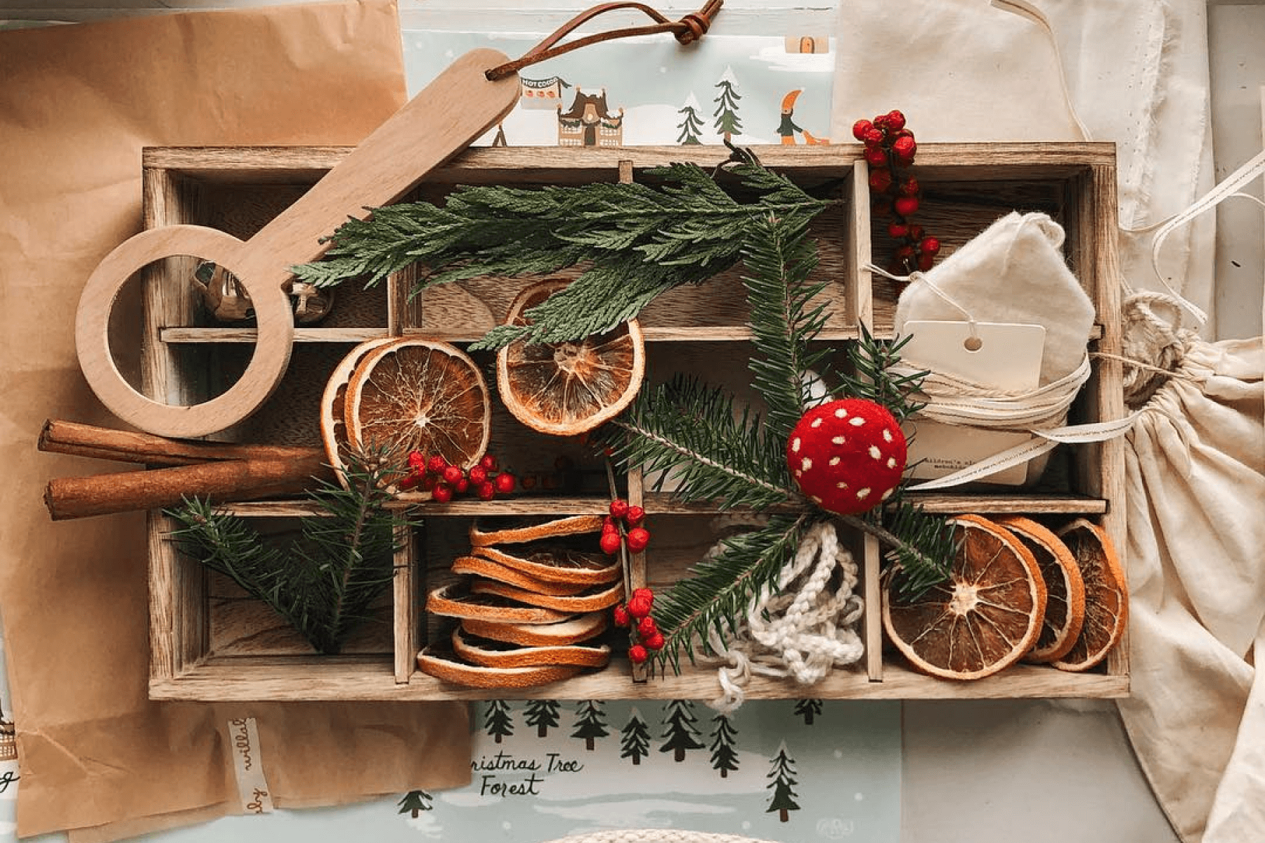 An overhead photograph of a wooden box filled with gift tags, cinnamon stick, orange slices, and greenery.