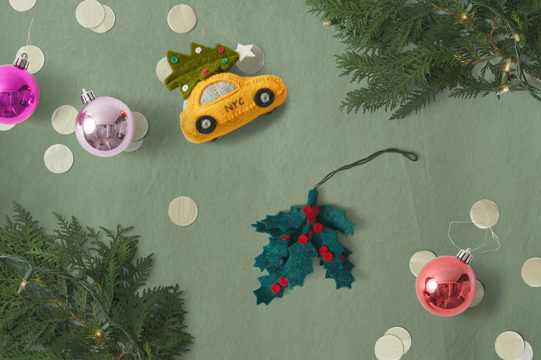 Holiday ornaments available at Party Shop: Yellow taxi and holly sprig by Craftspring. The items are surrounded by greenery, confetti, and bulb-shaped ornaments.