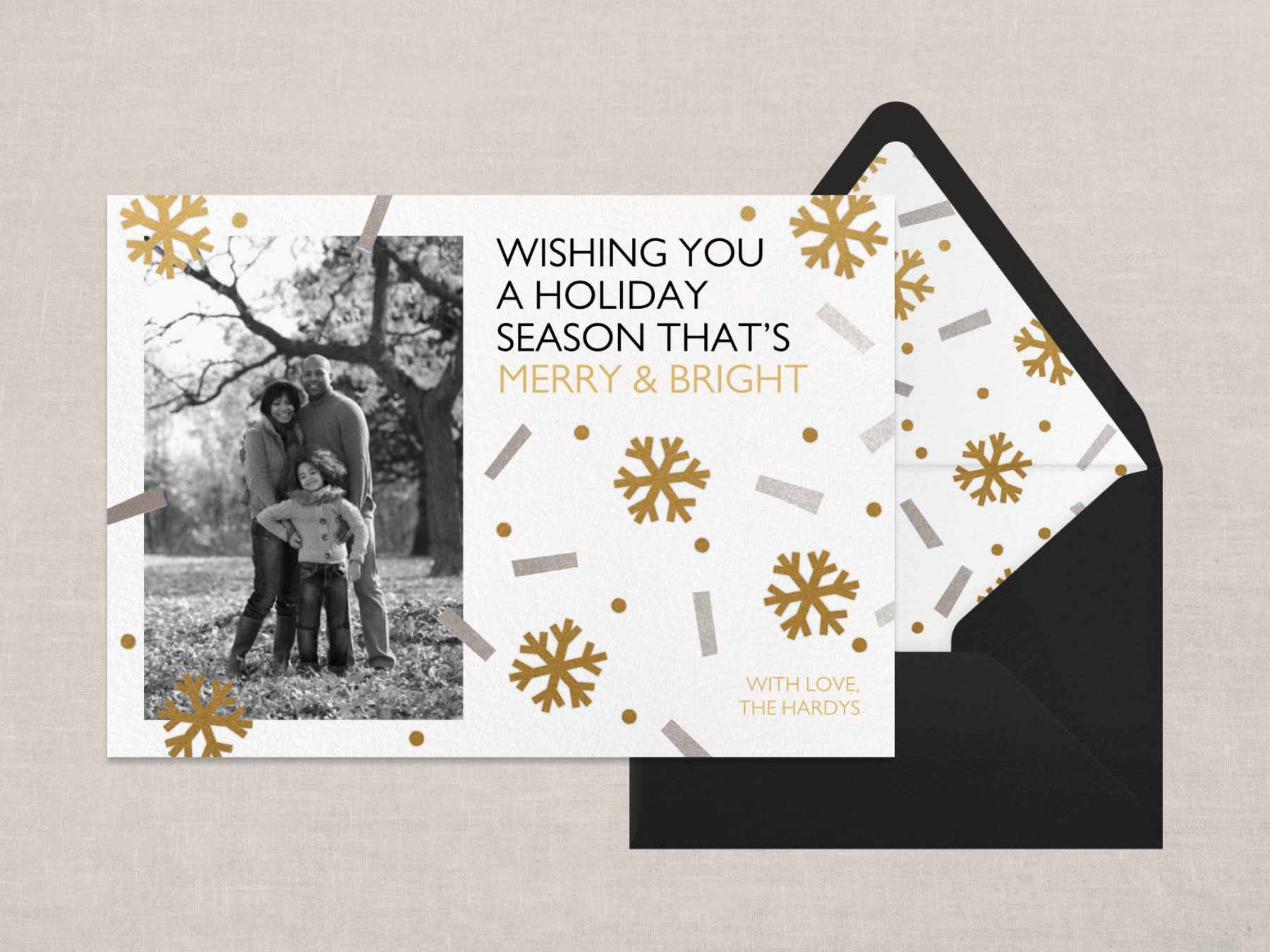 A holiday card with a vertical black and white photo on the left side and gold snowflakes and silver confetti.