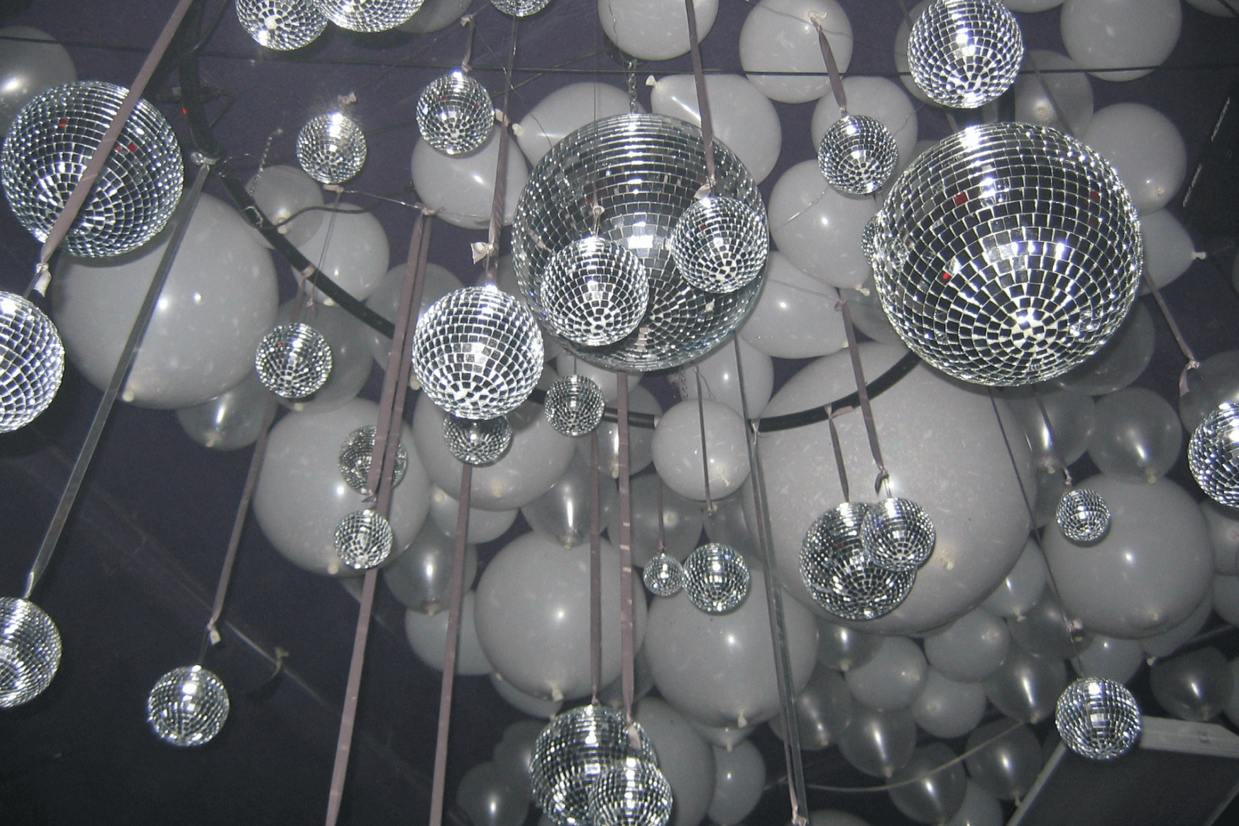 A view from below of multi-sized disco balls and shimmery white balloons hanging from the ceiling.