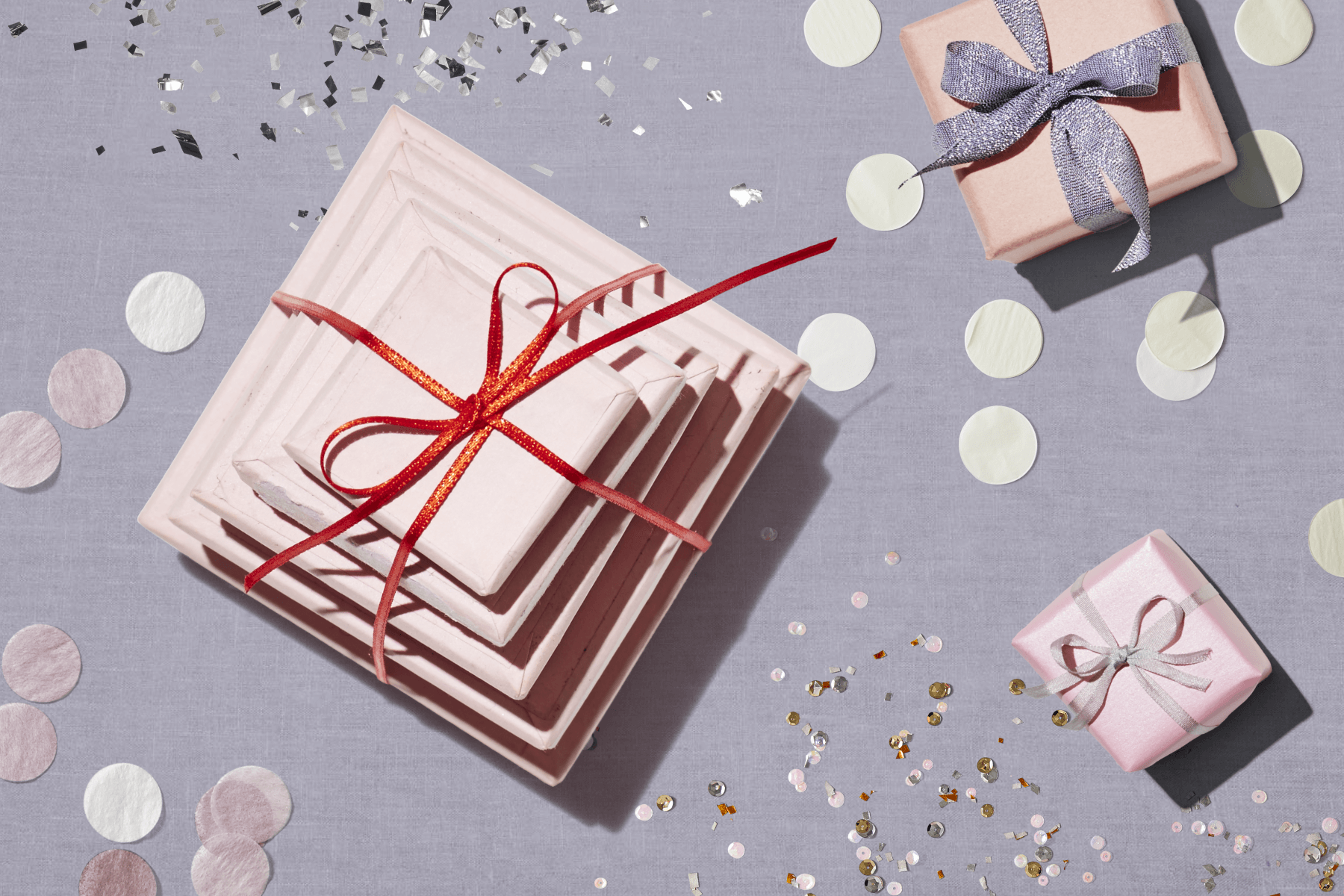 Stacks of light pink-wrapped presents tied with bows among glitter and large pastel confetti circles.