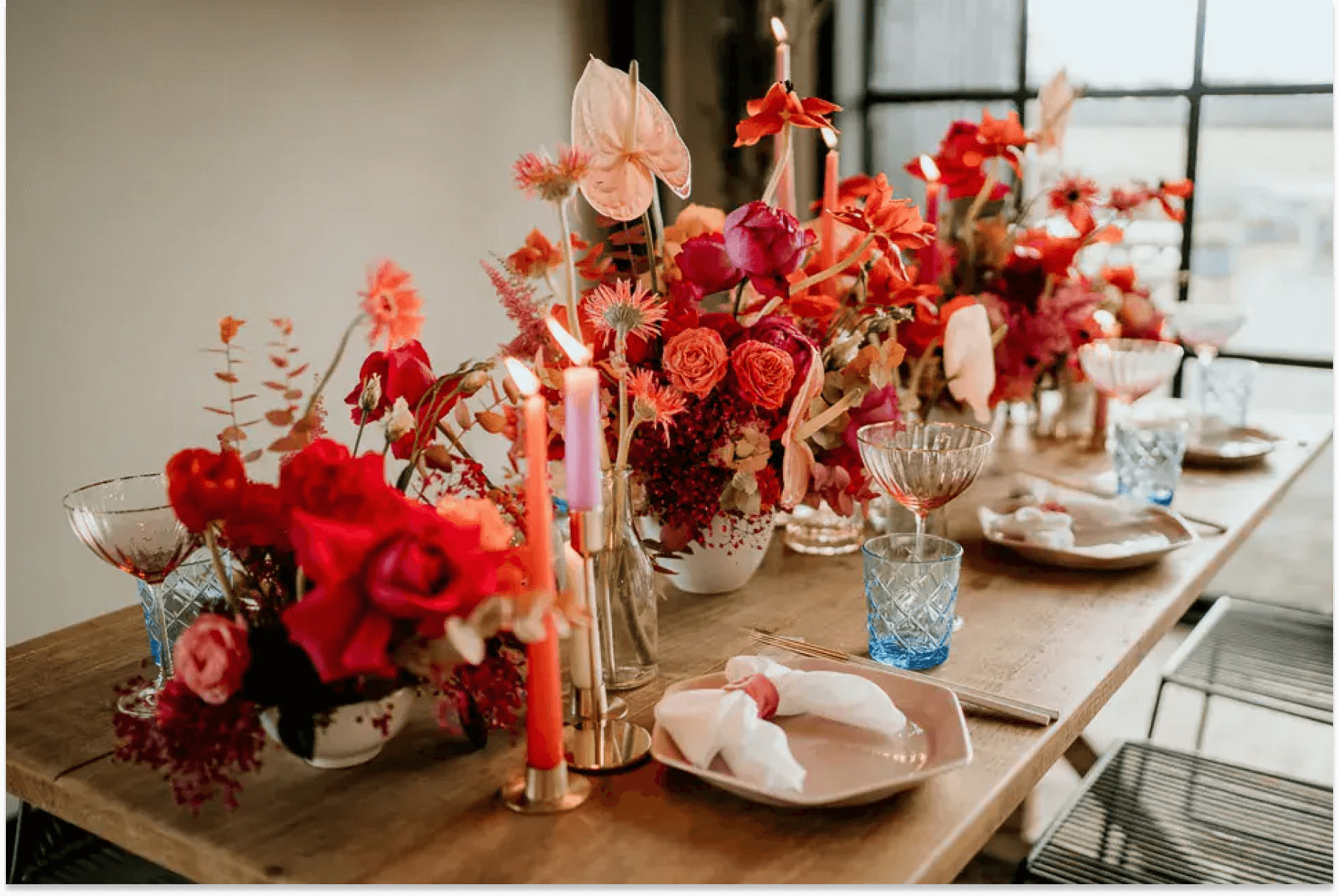 Bright red and pink floral design on a bare wooden table set with pink and blue dishware.