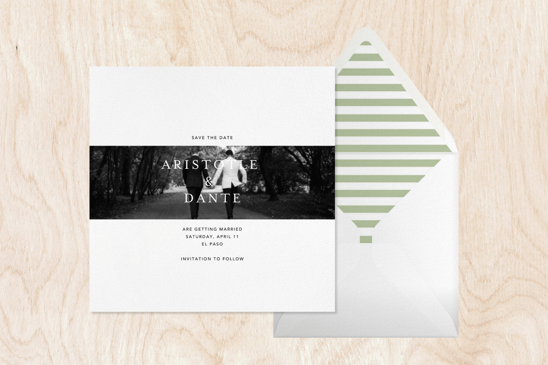 A simple save the date with a black and white photo of a couple extending in a stripe across the card, next to a white envelope with a green and white striped liner on a light wood grain backdrop.
