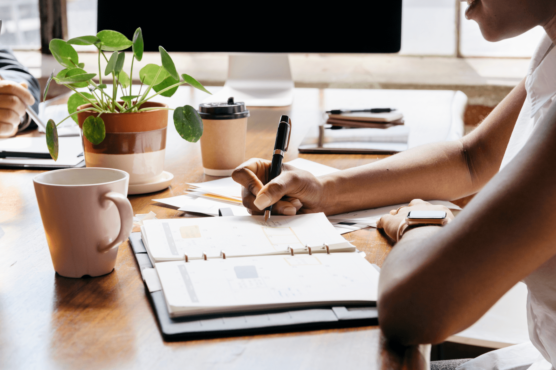 A person writes in an agenda book at a desk.