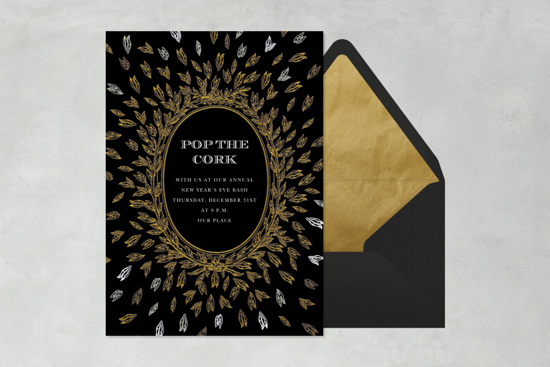 A black card with a gold oval frame and delicate leaves flying out from the center and the words “Pop the cork.”