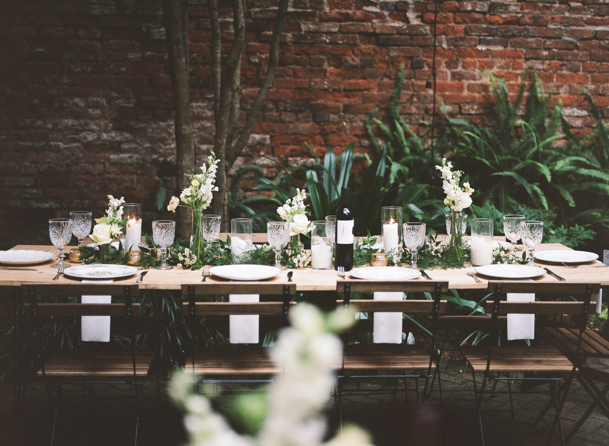 An outdoor dinner party set with elegant decor including crystal wine glasses and white flowers.