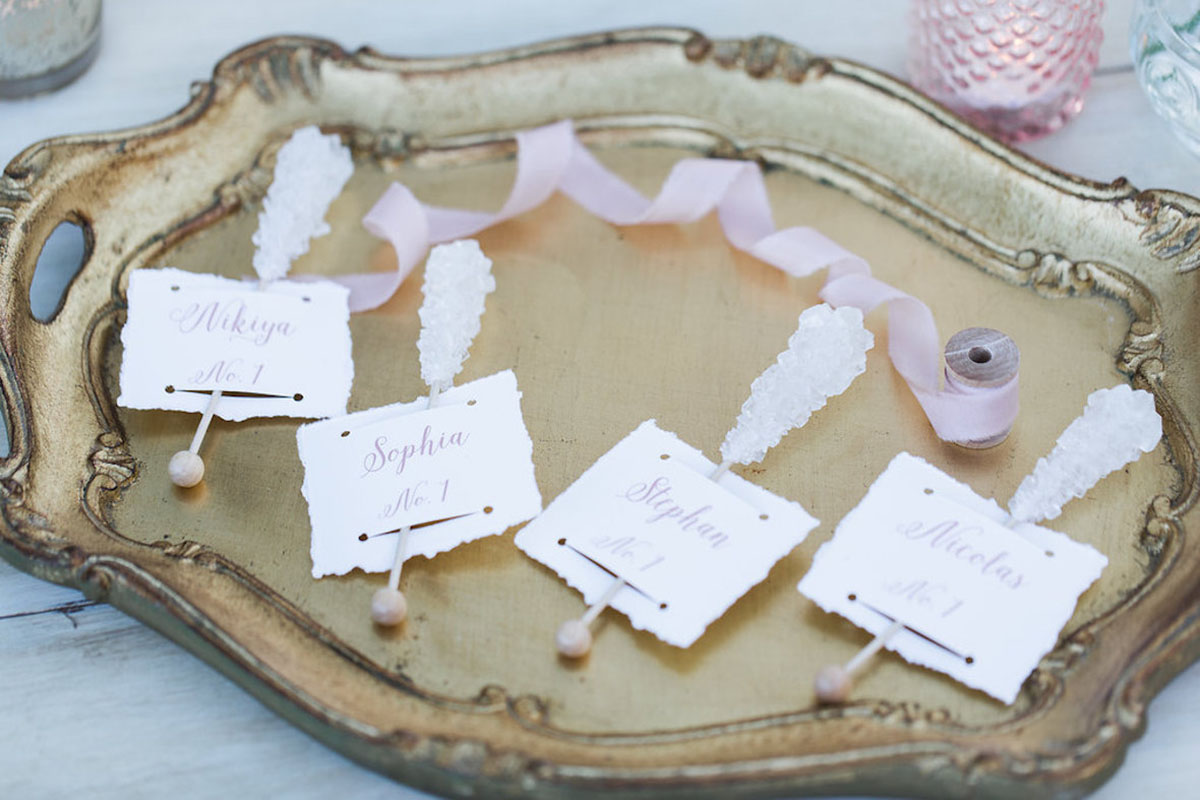 Party place cards attached to rock candy sticks with a pink spool of ribbon.