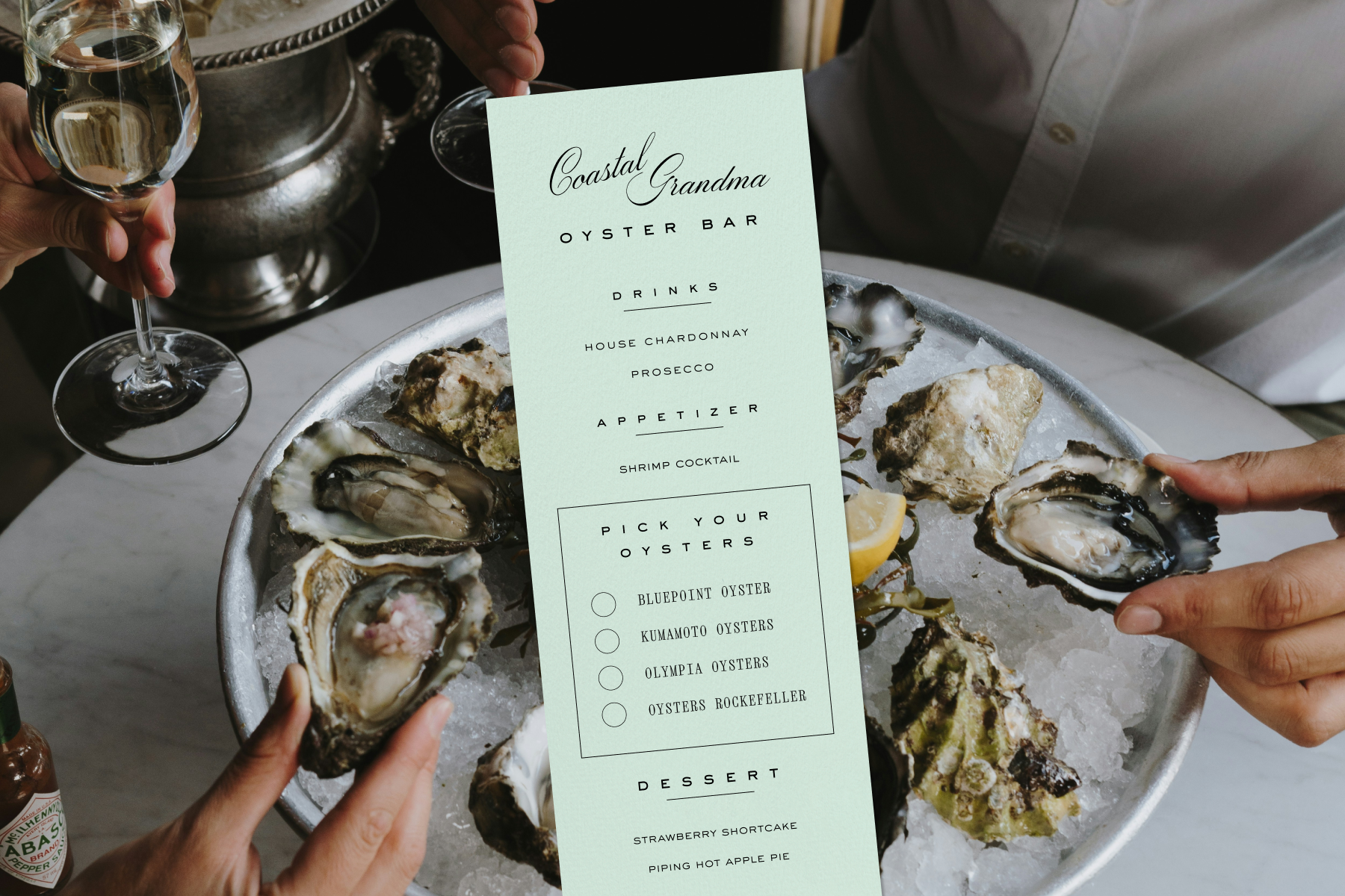 A menu for a Coastal Grandma oyster bar sits over an image of oysters on ice and wine glasses held over a white marble table.