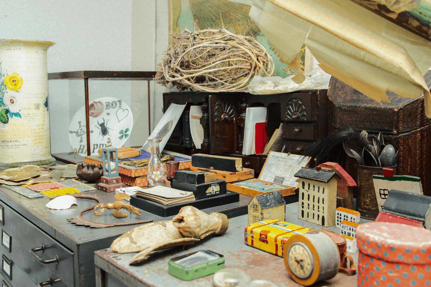 Inside John Derian's studio, a table topped with ephemera and collected items including old boxes, toy houses, and papers .