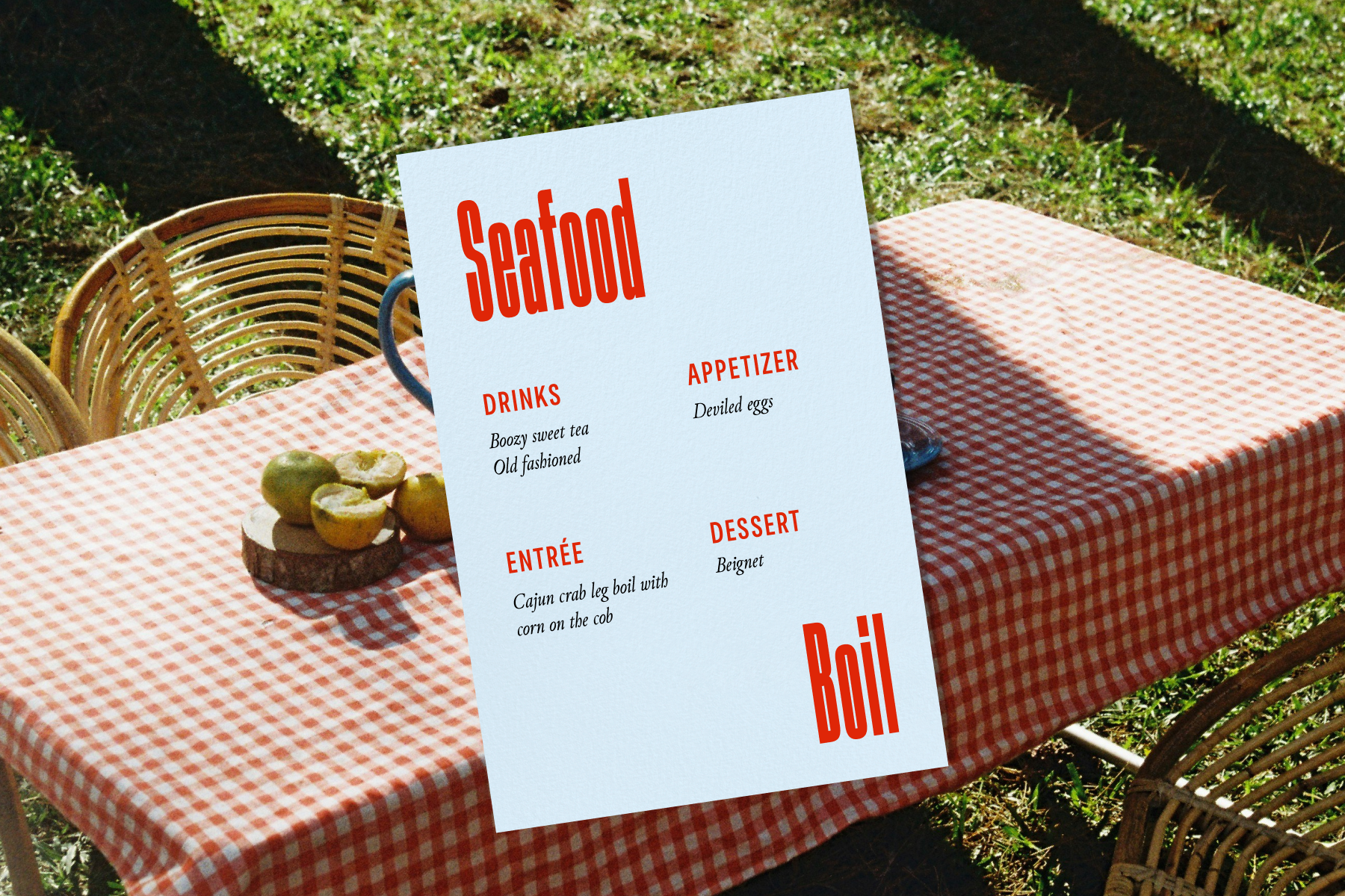 A light blue seafood boil menu with red text sits over a background image of an outdoor table on grass set with a red and white gingham tablecloth.