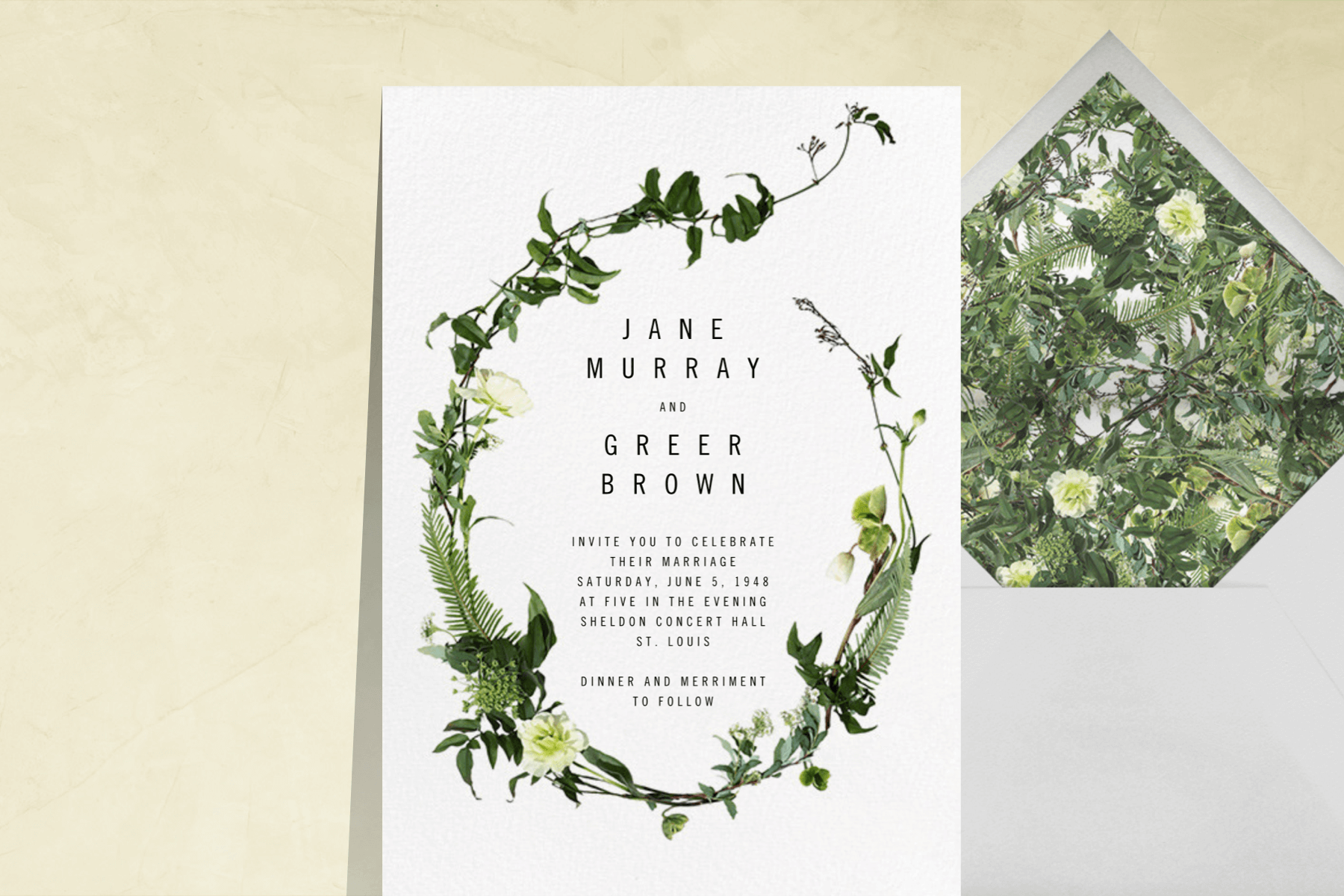 A white wedding invitation with a swoosh of greenery and florals around the text.