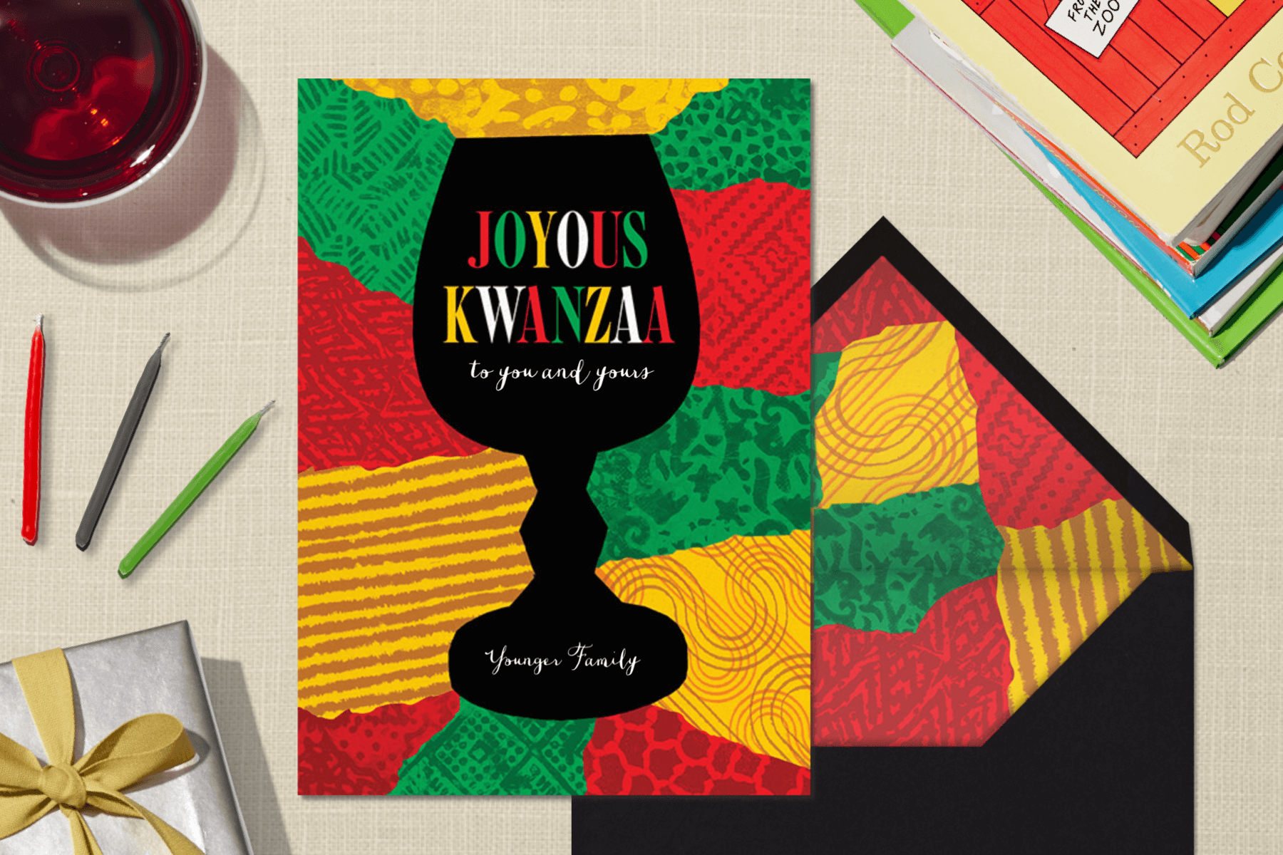A Kwanzaa invitation surrounded by wine, candles, and books.