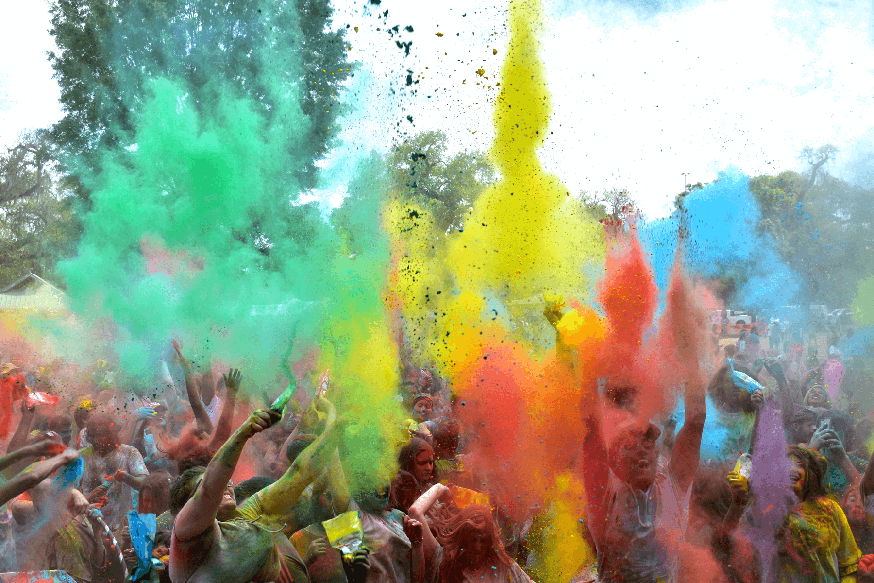 Close up photo of a group of revelers throw colors in the air at a Holi celebration.