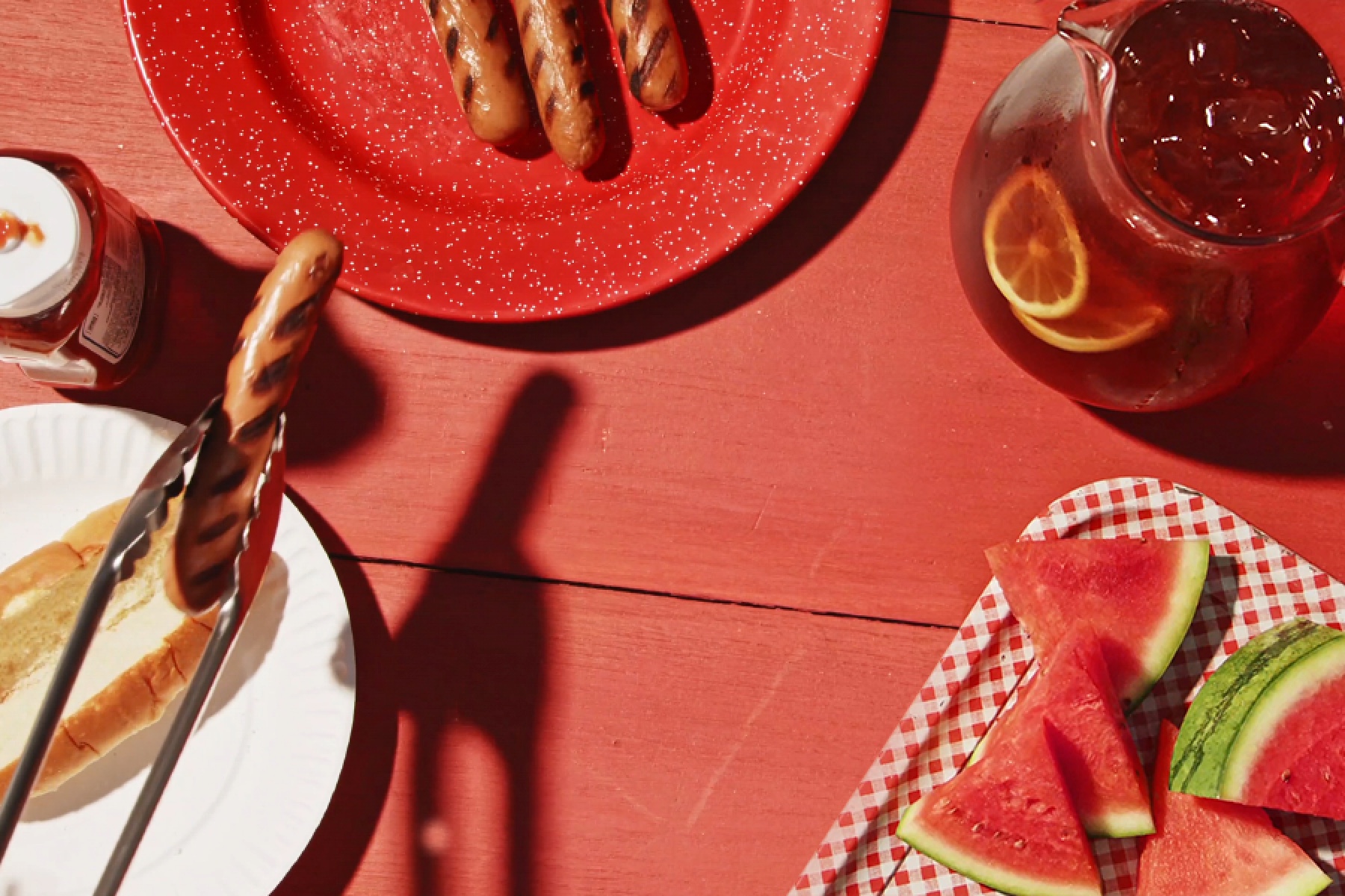 Picnic table with hot dogs and watermelon.