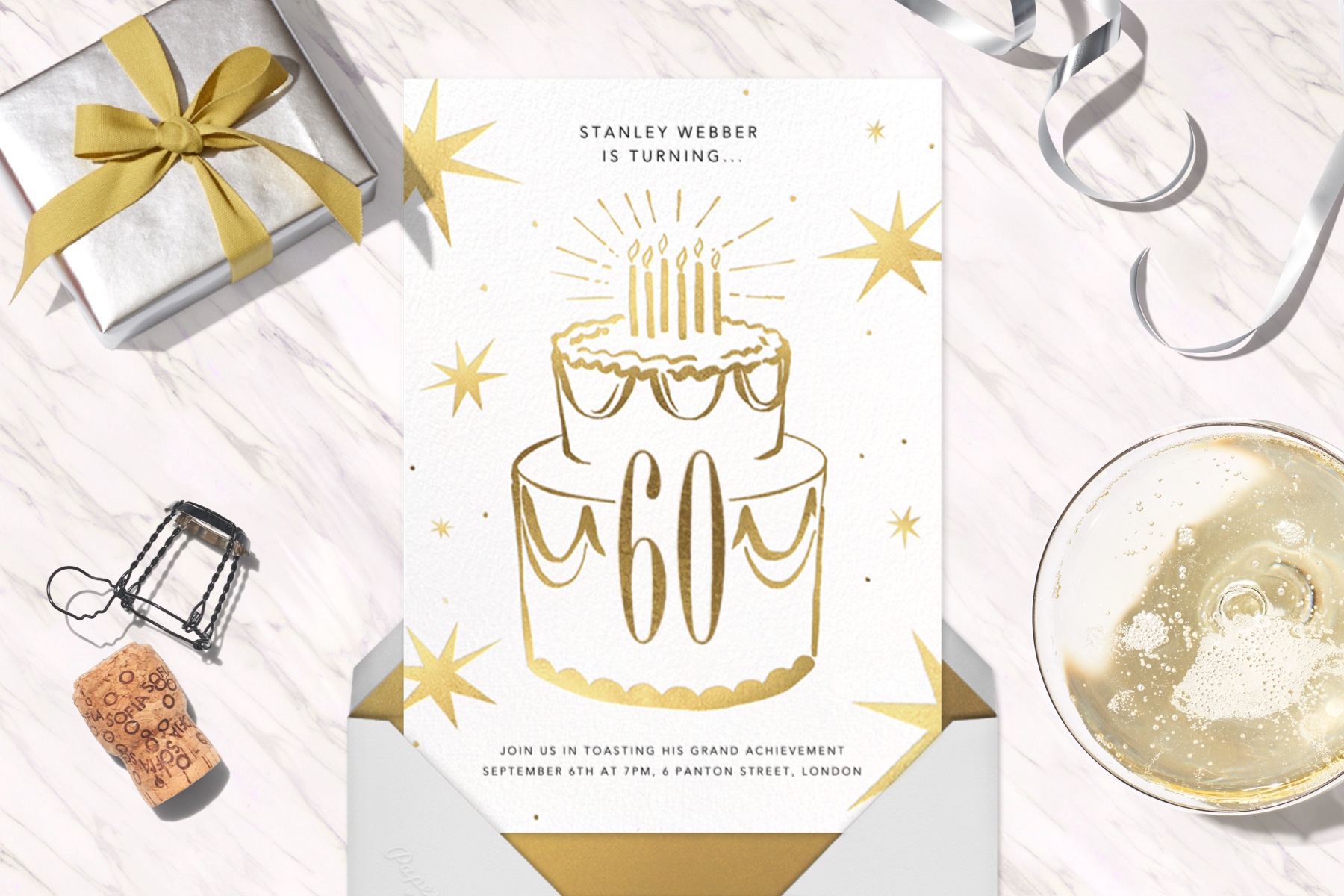 “Big Year” invitation by Paperless Post, featuring an illustration of a big cake with the number “60” on it. The card is surrounded by party goods like a present, cork, and champagne.