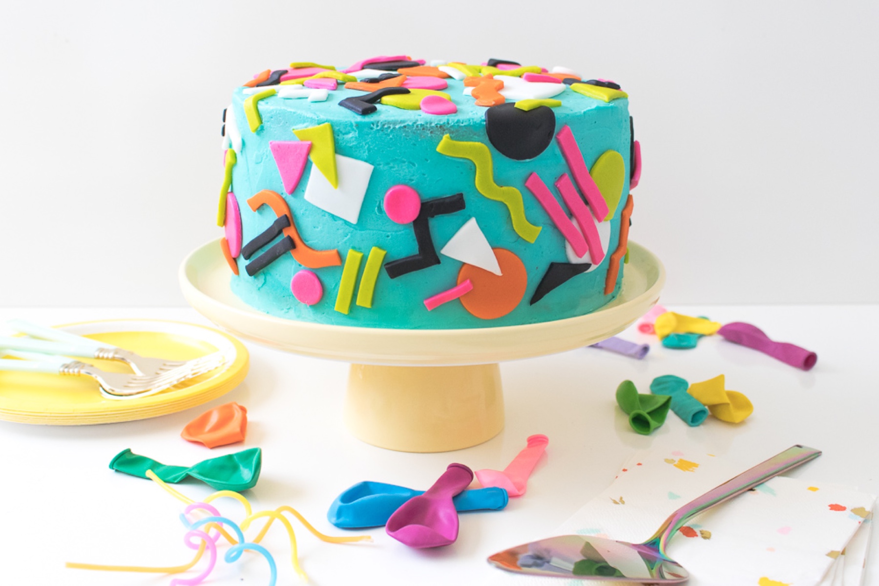 A blue cake decorated with bright Memphis-style geometric shapes.