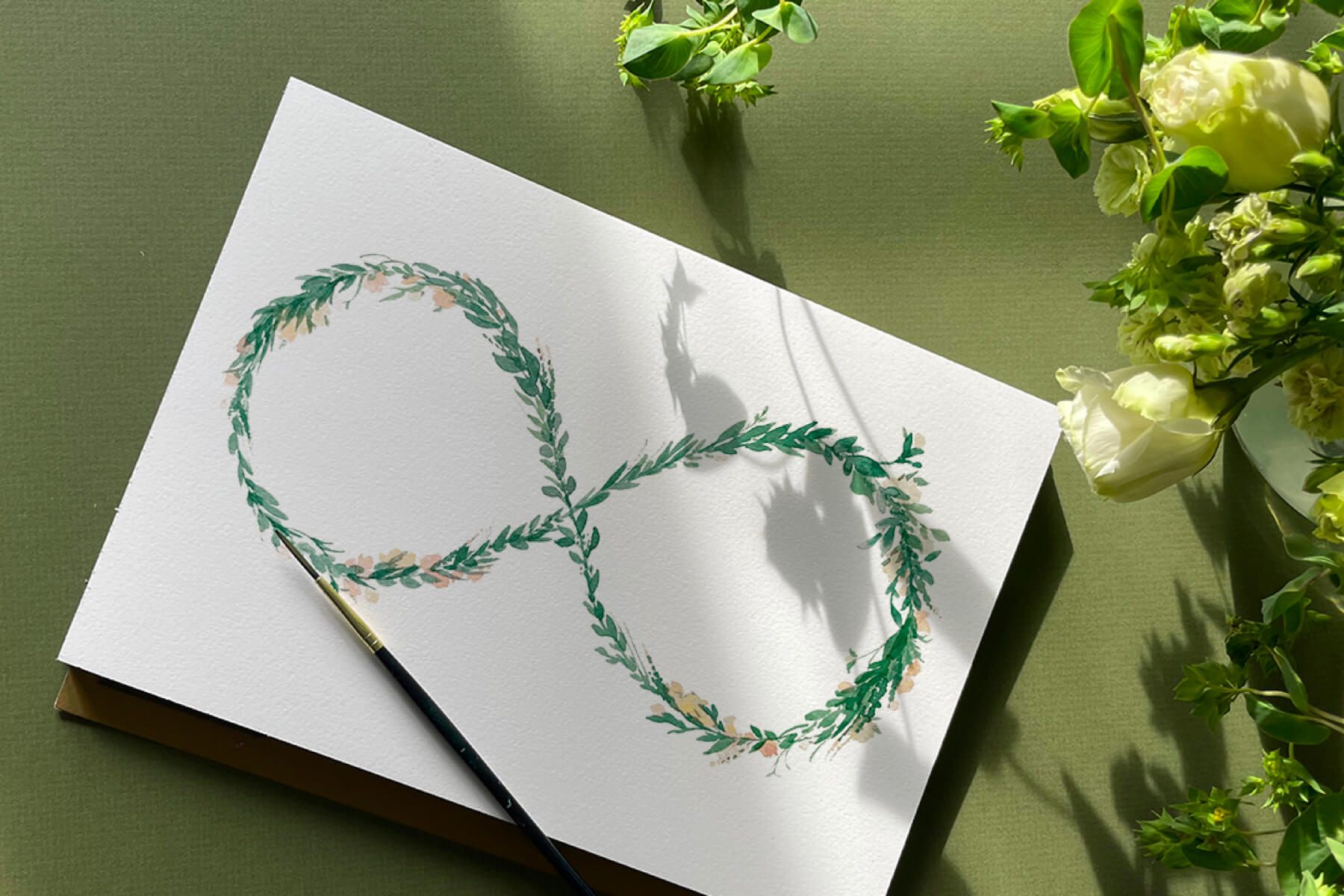 Photo of a handpainted card with a floral infinity sign surrounded by paintbrush and flowers.