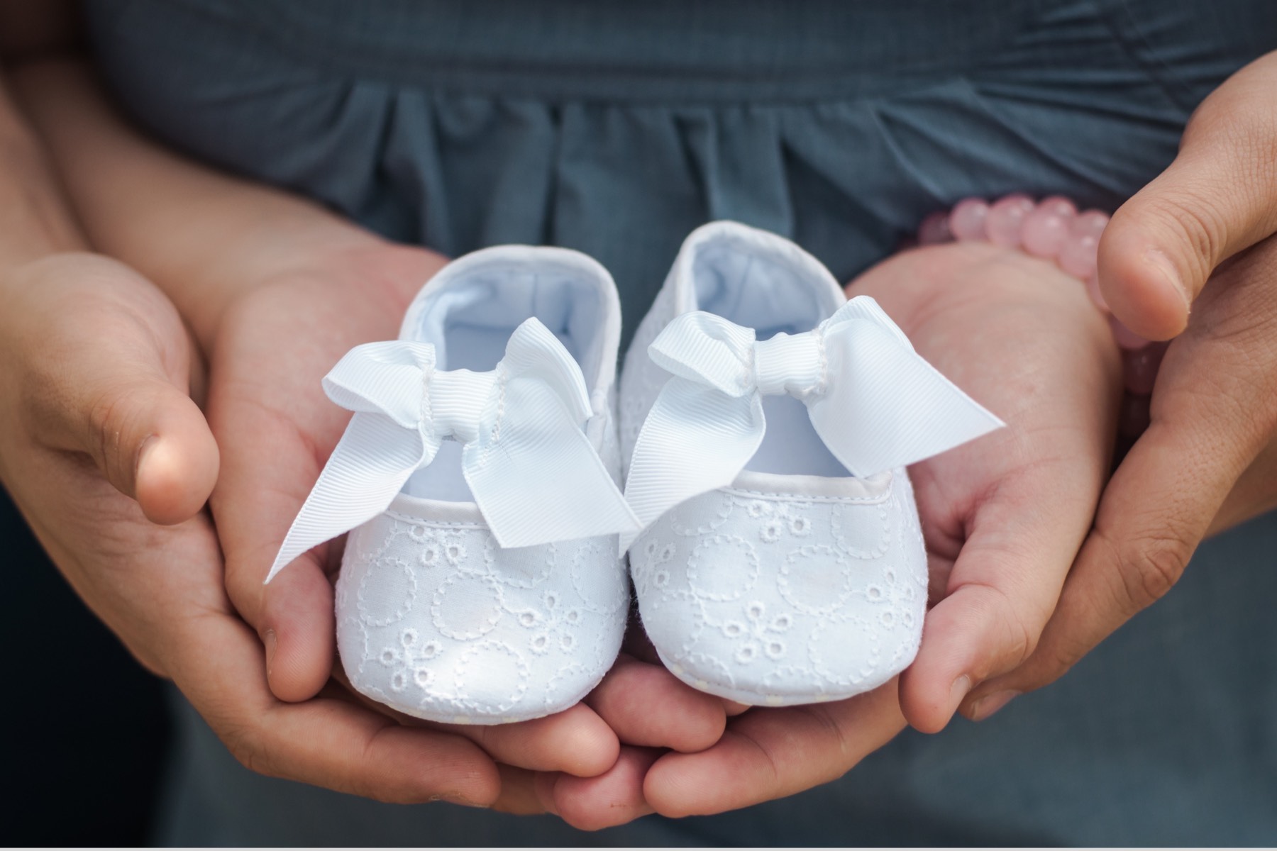 Close up of hands holding white baby shoes.