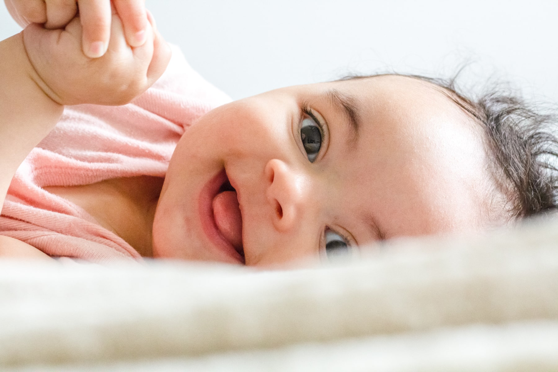 Close-up photo of a baby laying down and smiling at the camera.