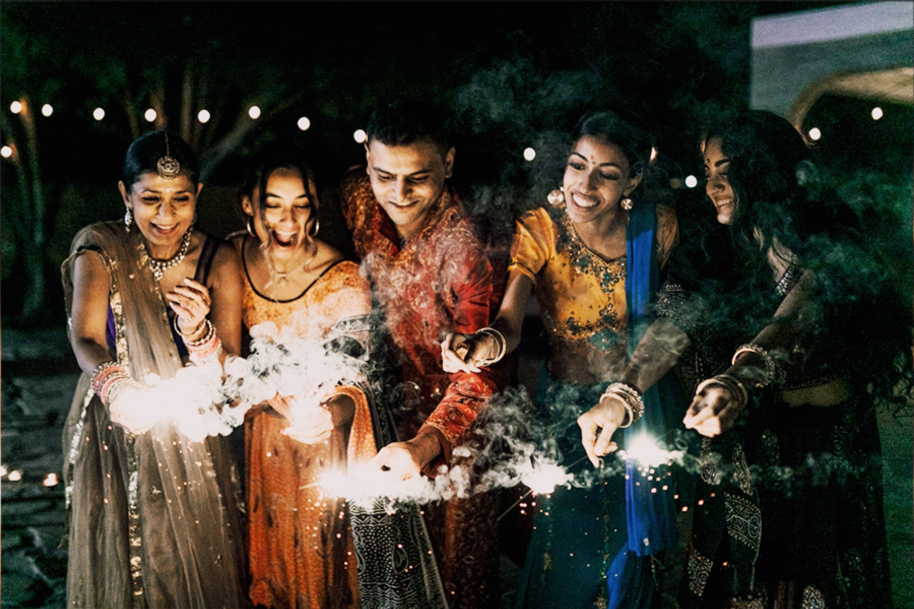 A group of festively dressed people lighting sparklers.