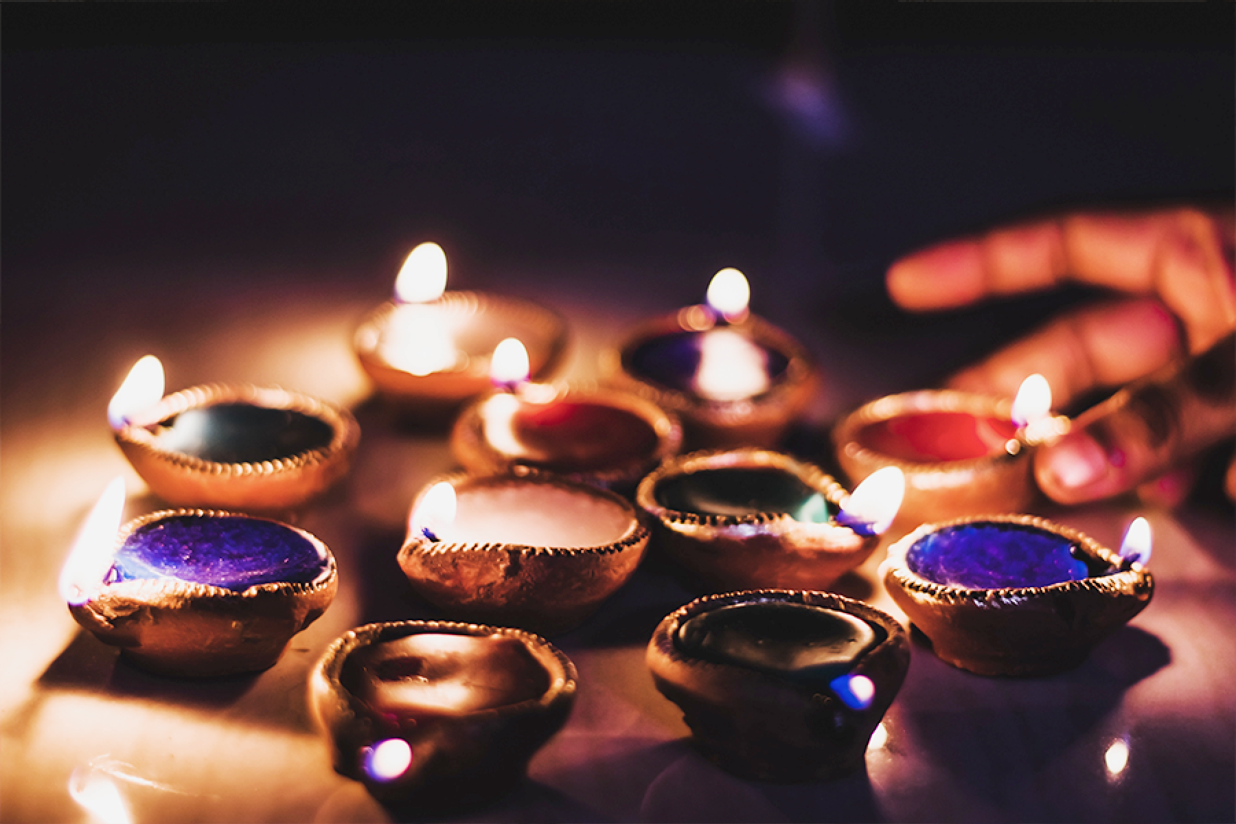 A hand placing lit diyas together.