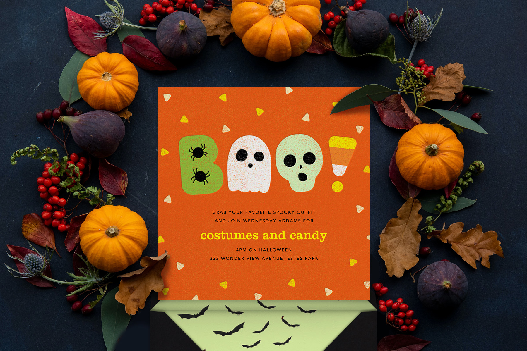 “Candy Dandy” invitation by Paperless Post. Orange card featuring an illustration of the word “Boo!” made out of spiders, a ghost, a skeleton, and a candy corn. The dark background is accented with a beautiful autumnal wreath of gourds, berries, and leaves.