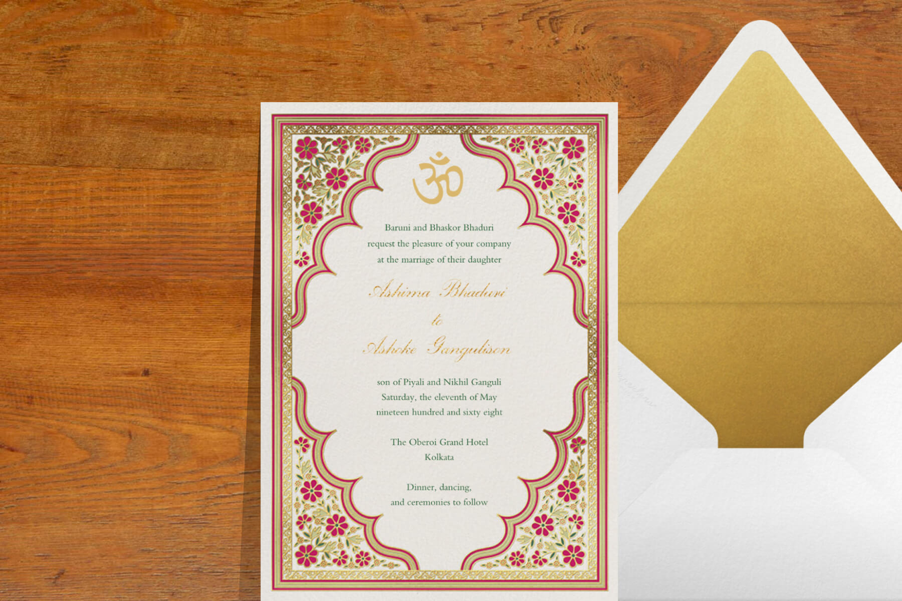 An Indian wedding invitation featuring Indian art motifs like flowers and ornate borders. The card is paired with a white envelope with a gold lining.