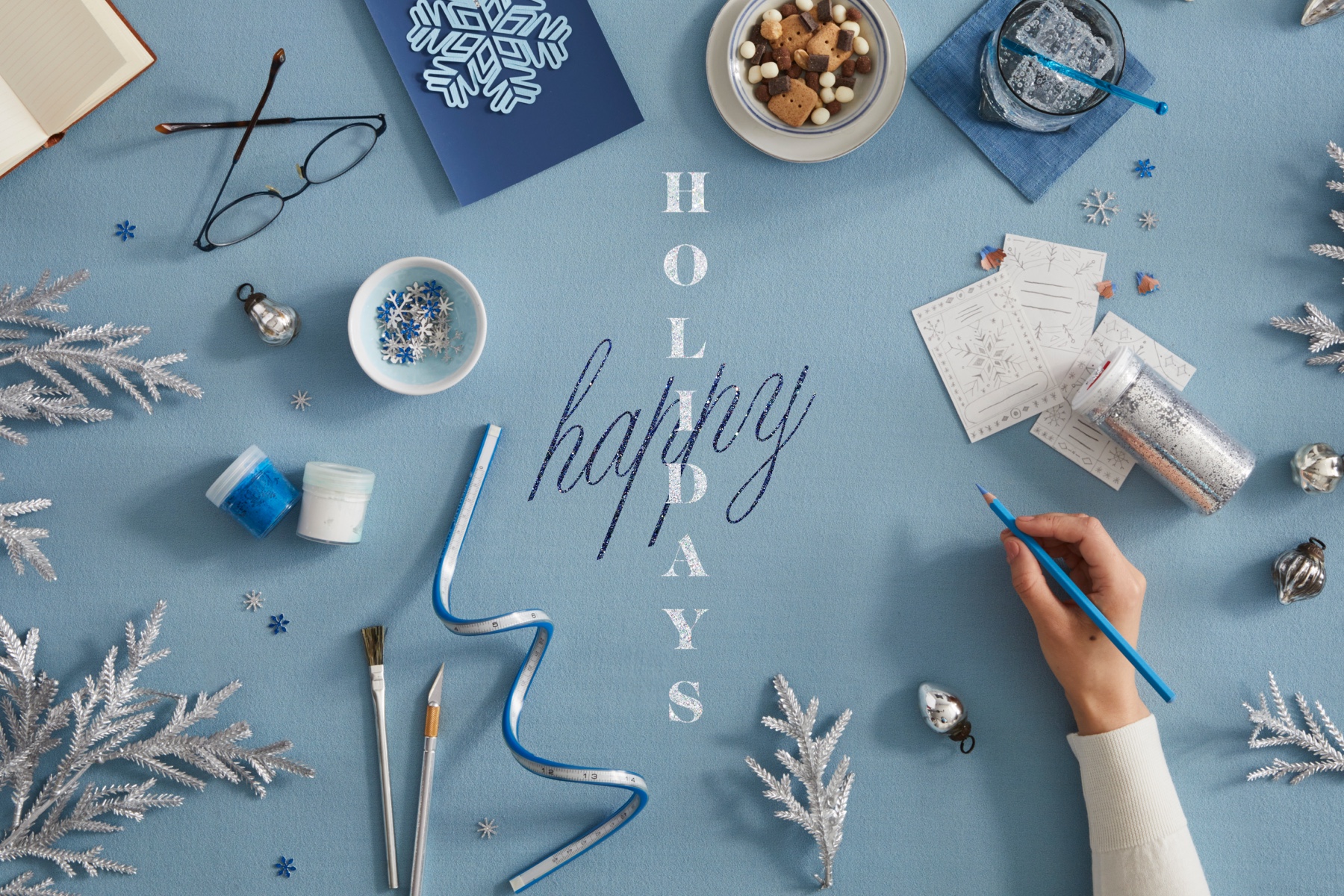 Overhead photo of an artist’s hand sketching holiday items and designs.