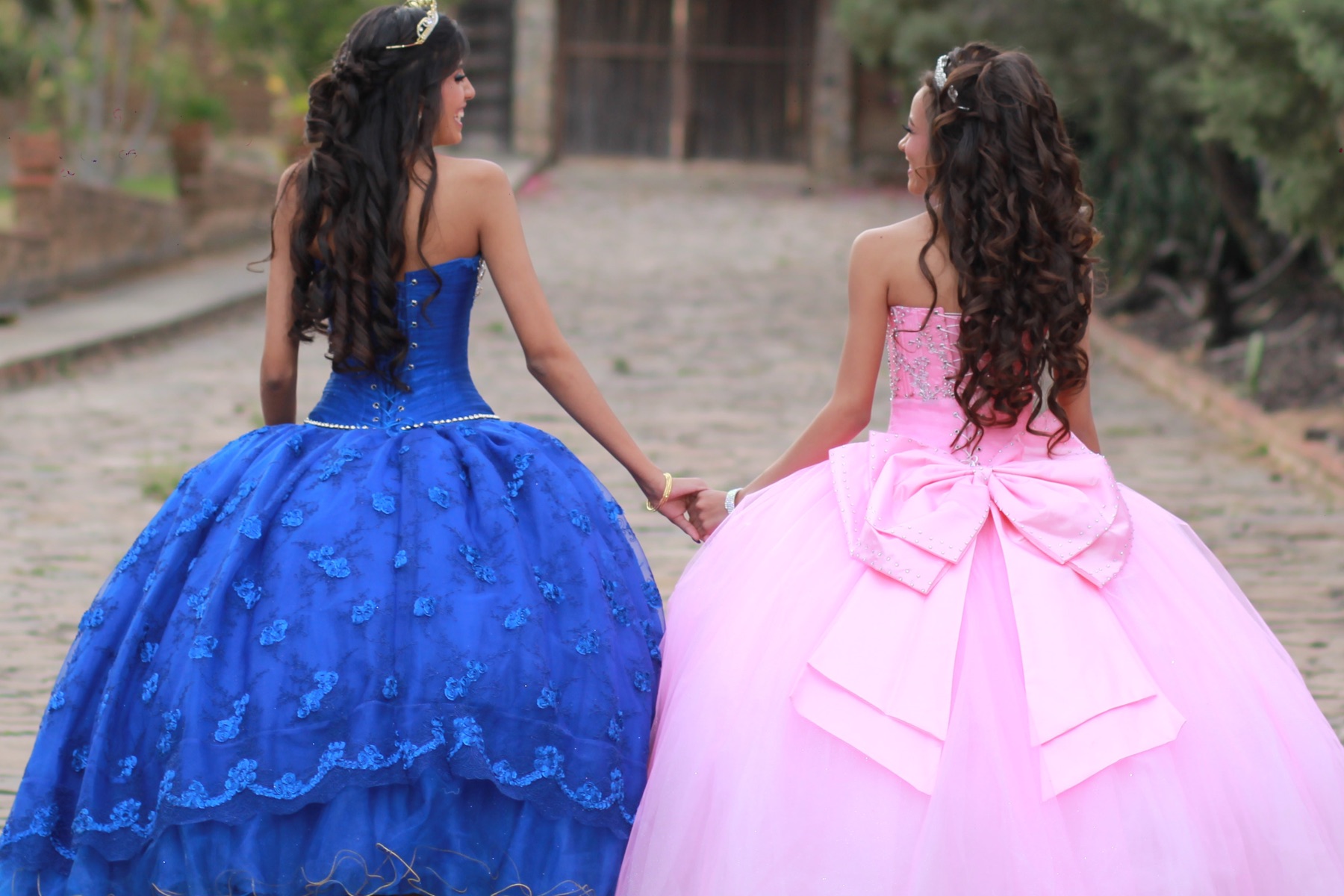 Photo of two young girls holding hands and wearing blue and pink ball gowns