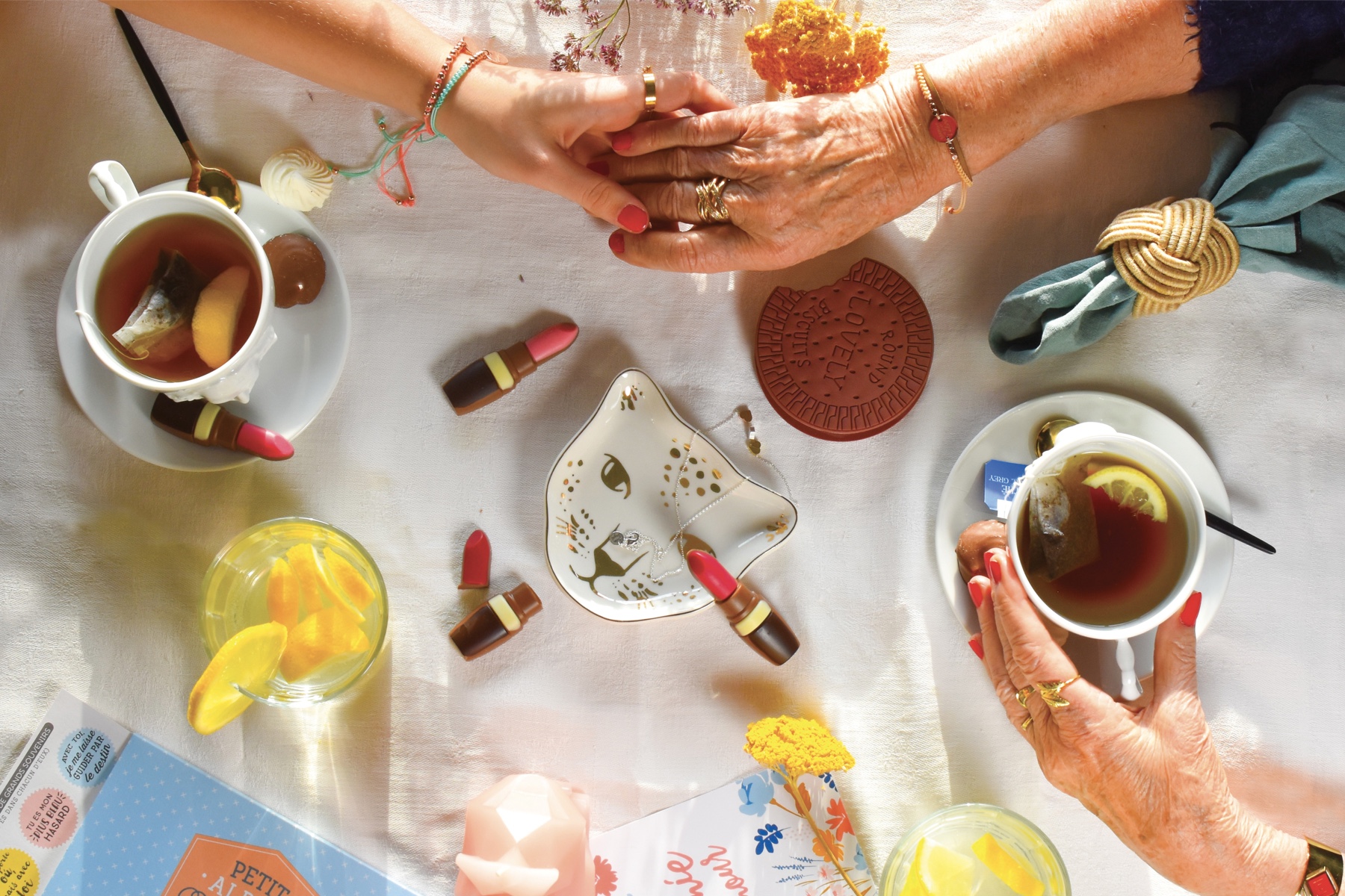 Overhead photo of a tea party in progress, including two hands clasping, tea cups, and snacks.