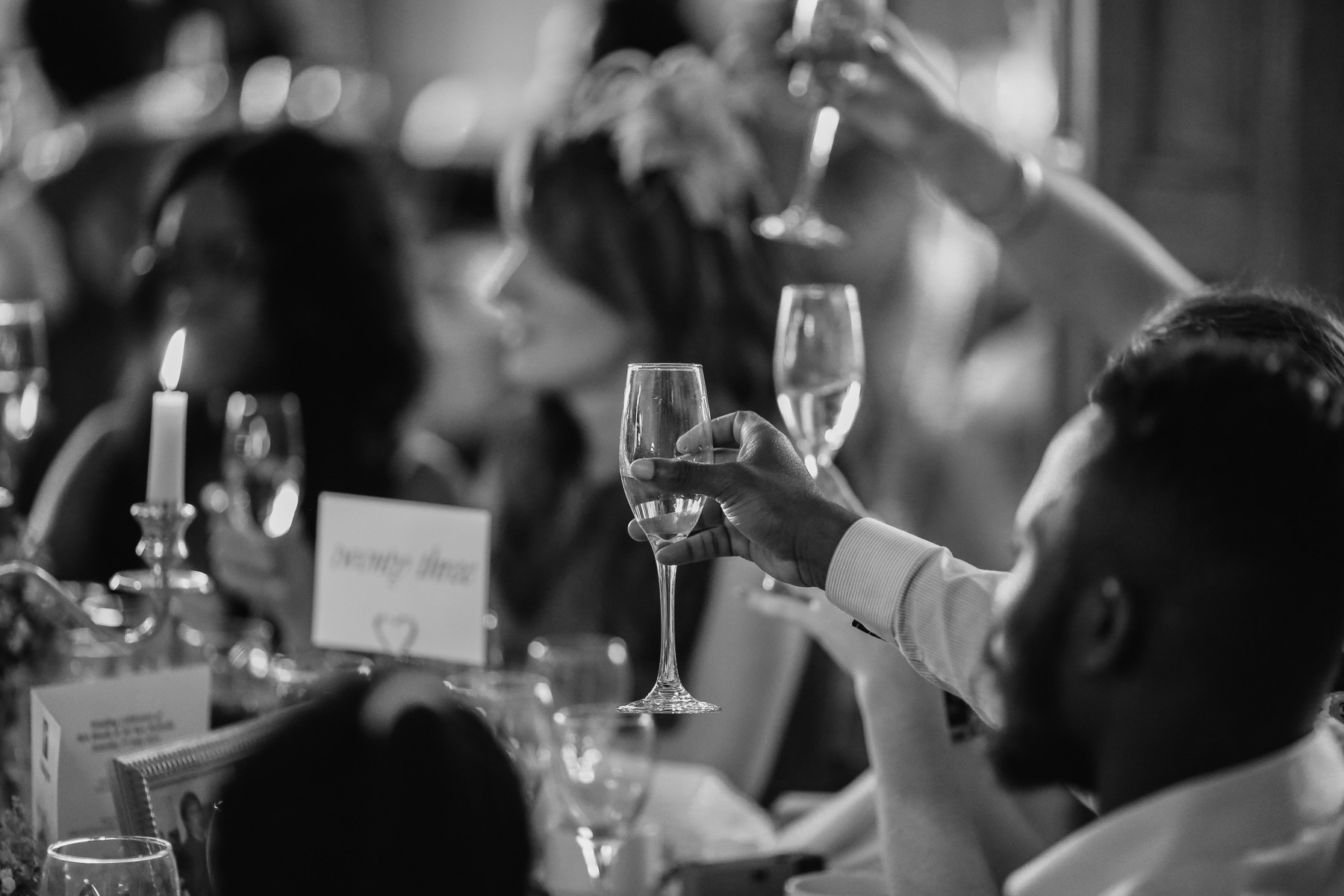 Soft focus black and white photo of guests holding up their champagne glasses for a toast.