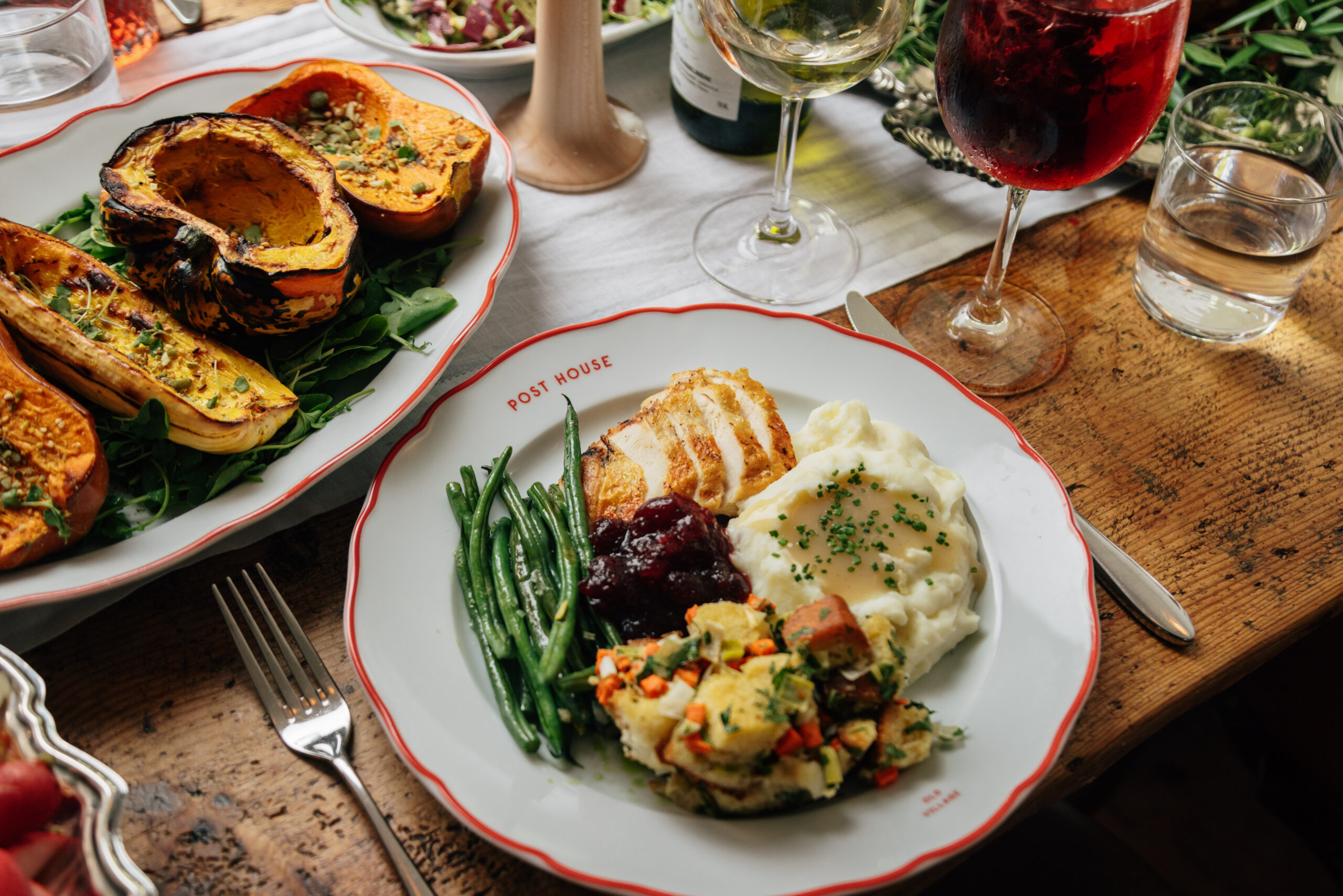 Plate of mashed potatoes, green beans, turkey, cranberries, and stuffing on a Thanksgiving table. 